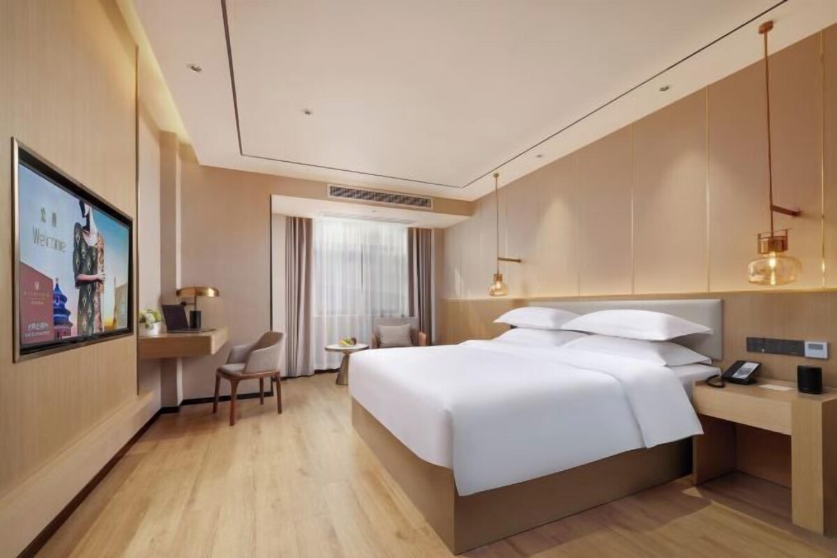 A modern hotel room with a large bed, a desk, a chair, and a TV on the wall.