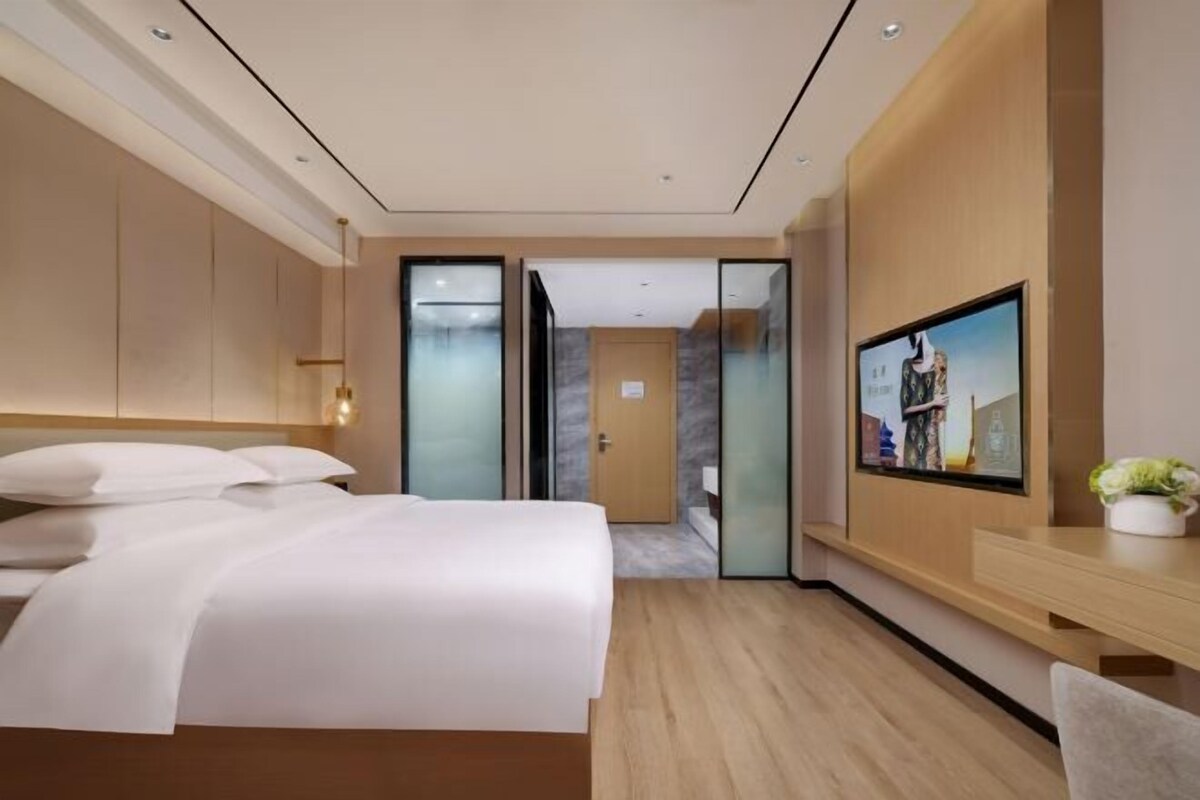 A modern hotel room with a large bed, a desk, and a television on the wall.