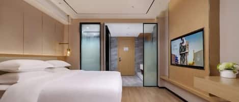A modern hotel room with a large bed, a desk, and a television on the wall.