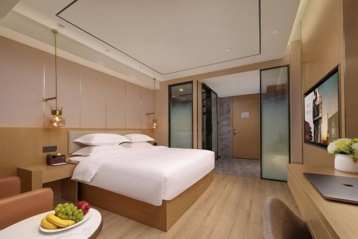 Una habitación de hotel moderna con una cama grande, un escritorio con una computadora portátil, una bandeja de frutas y un televisor en la pared.