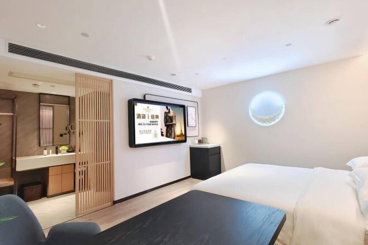 Una habitación de hotel con cama, escritorio, espejo, armario y televisor de pared.