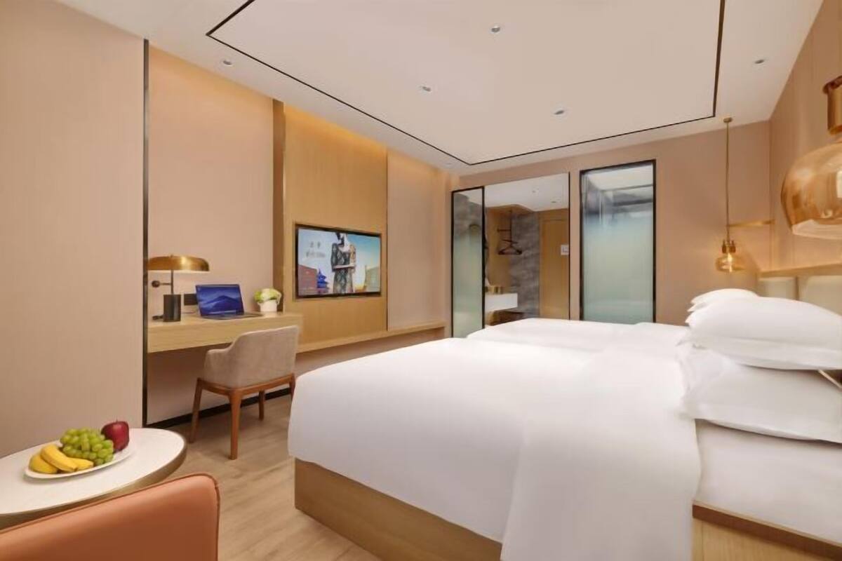 Una habitación de hotel moderna con una cama grande, un escritorio con una silla, una mesita con fruta y un espejo amplio.