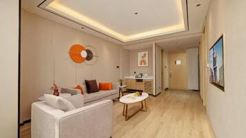 Una habitación de hotel moderna con sofá, una pequeña mesa redonda, zona de cocina y un pasillo que conduce a otra habitación.