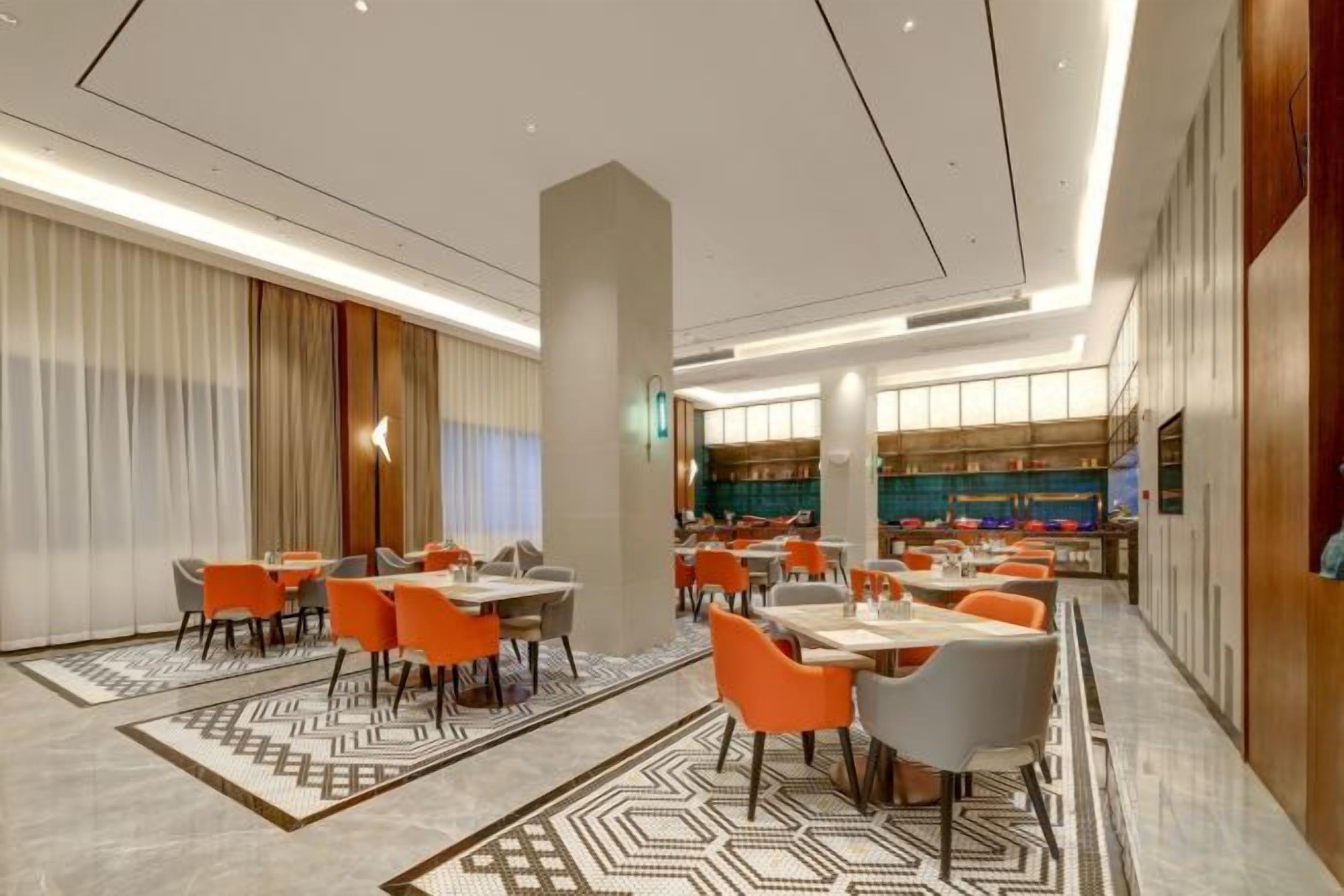 A modern hotel dining area with multiple tables and chairs, a patterned rug, and a large pillar.
