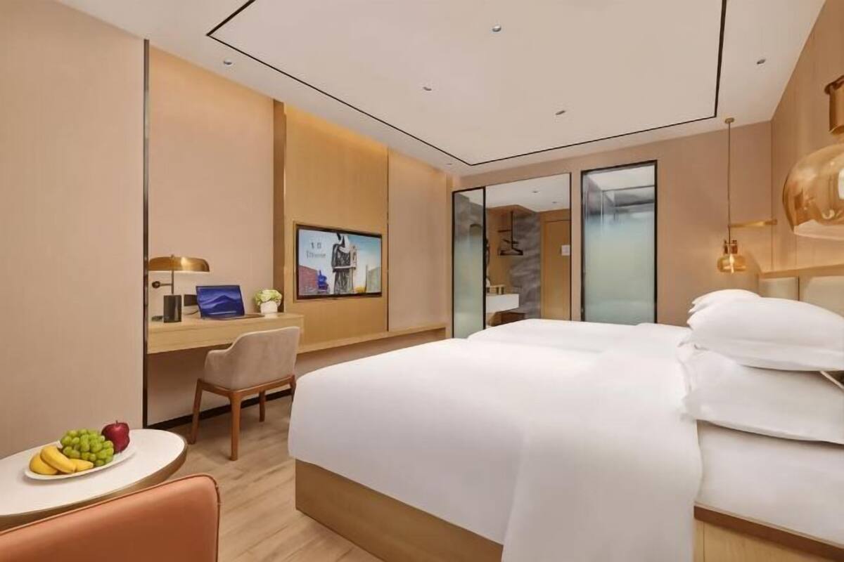 Habitación de hotel con cama, escritorio, silla y una pequeña mesa con fruta.