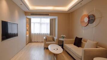 Habitación de hotel moderna con sofá, una mesita redonda, televisión y ventana con cortinas.