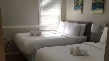 A hotel room with two single beds, a window with blinds, a small table, and a chair.