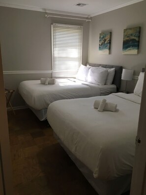 A hotel room with two single beds, a window with blinds, a small table, and a chair.