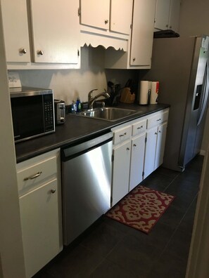 A compact kitchen with white cabinets, a stainless steel refrigerator, a microwave, and a dishwasher.