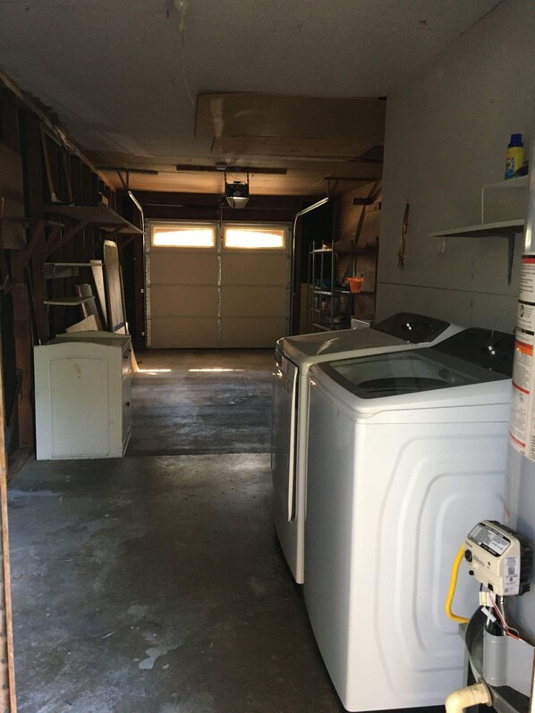 A laundry room with two washing machines, a dryer, and a utility room with a water heater and a white cabinet.