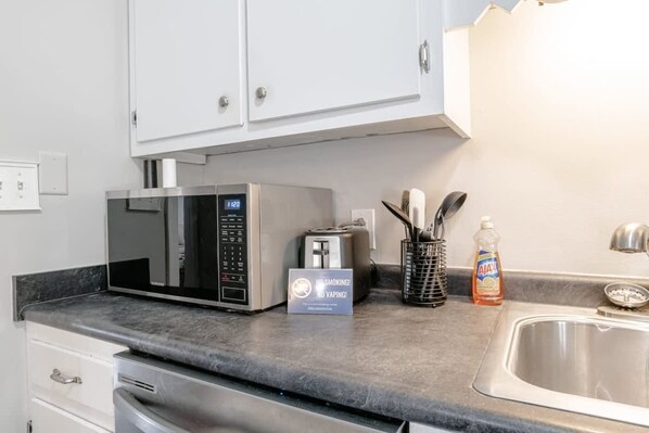A kitchen with a microwave, toaster, and a sign prohibiting smoking and vaping.