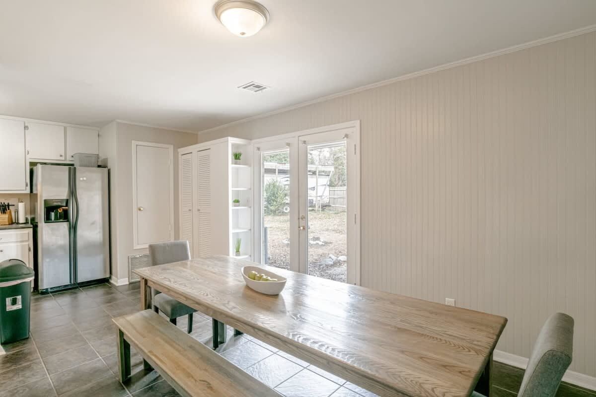 Une cuisine avec une table en bois, un banc et une vue sur l’extérieur grâce à des portes vitrées.
