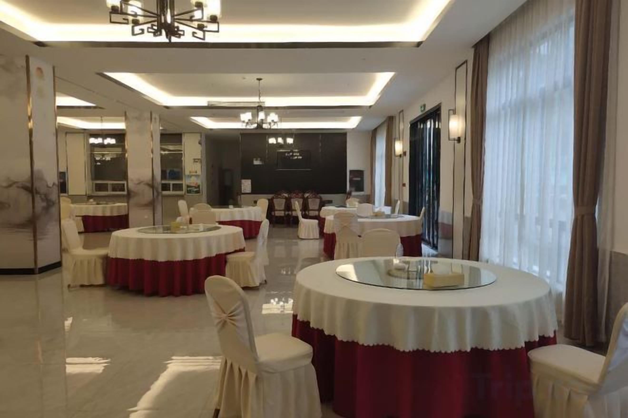 Uma sala de jantar de hotel com mesas redondas, cadeiras e um candelabro.