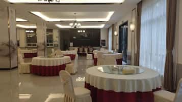 Uma sala de jantar de hotel com mesas redondas, cadeiras e um candelabro.