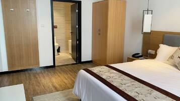 A hotel room with a bed, a wardrobe, a nightstand, and a door leading to a bathroom.