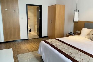 Une chambre d’hôtel comprenant un lit, une armoire, une table de chevet et une porte donnant accès à une salle de bain.