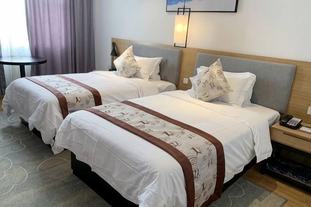 Quarto de hotel com duas camas, cada uma com cabeceira, mesas de cabeceira e luminária.