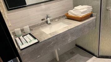 A modern bathroom with a marble sink, a glass shower enclosure, and a basket of folded towels.