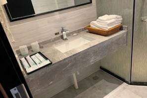 Une salle de bain moderne avec un lavabo en marbre, une cabine de douche en verre et un panier rempli de serviettes pliées.
