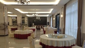 A spacious, well-lit dining area with round tables and chairs, large windows with curtains, and a modern chandelier. - Huashan Hotel (Government compound) (Ningming)