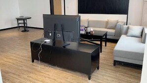 A modern living room with a flat-screen TV on a black stand, a grey sofa, a small round table, and a coffee table. - Huashan Hotel (Government compound) (Ningming)