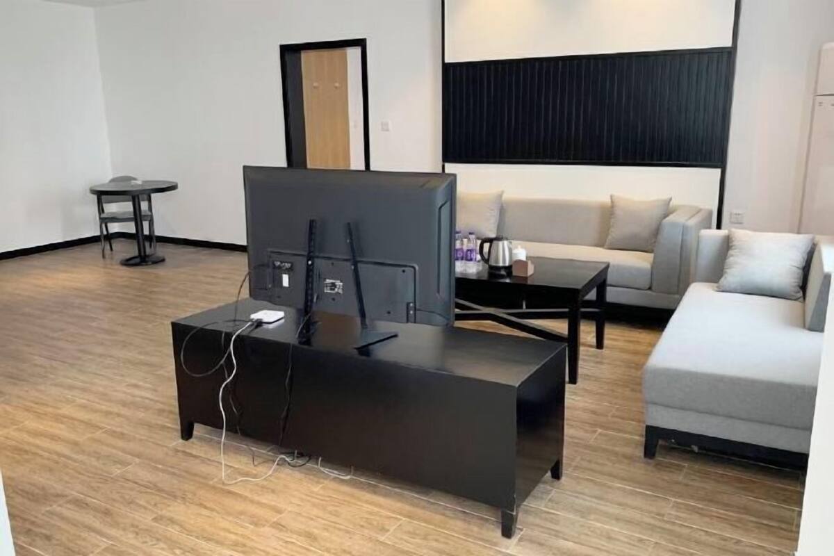 Uma sala de estar moderna com uma televisão de tela plana em um suporte preto, um sofá cinza, uma mesinha redonda e uma mesa de centro.