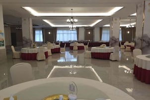 Un amplio salón de banquetes con mesas redondas, manteles blancos y rojos, y un candelabro.