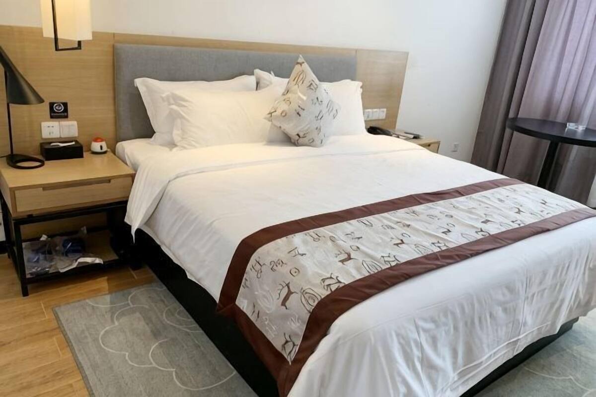 Quarto de hotel com cama, mesa de cabeceira, luminária e uma pequena mesa.