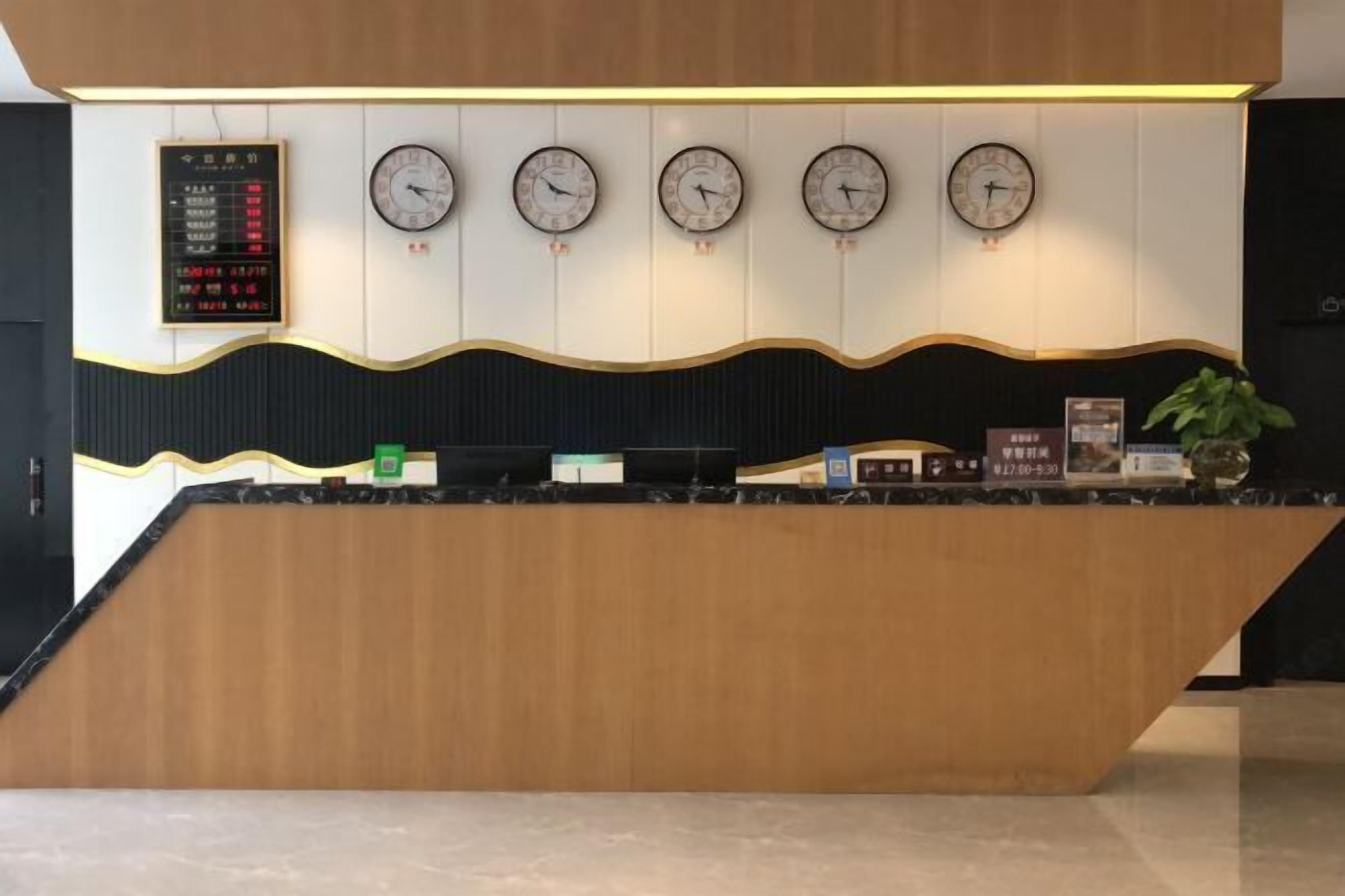 A reception desk with a wooden finish and a black countertop. There are five wall clocks above the desk, and a digital display board to the left.