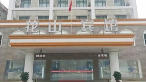 A hotel entrance with a large sign above the doors, potted plants on either side, and a flag on top. - Huashan Hotel (Government compound) (Ningming)