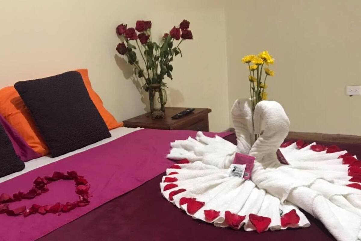 A bed with a purple bedspread, a white towel arrangement, and two vases with flowers.