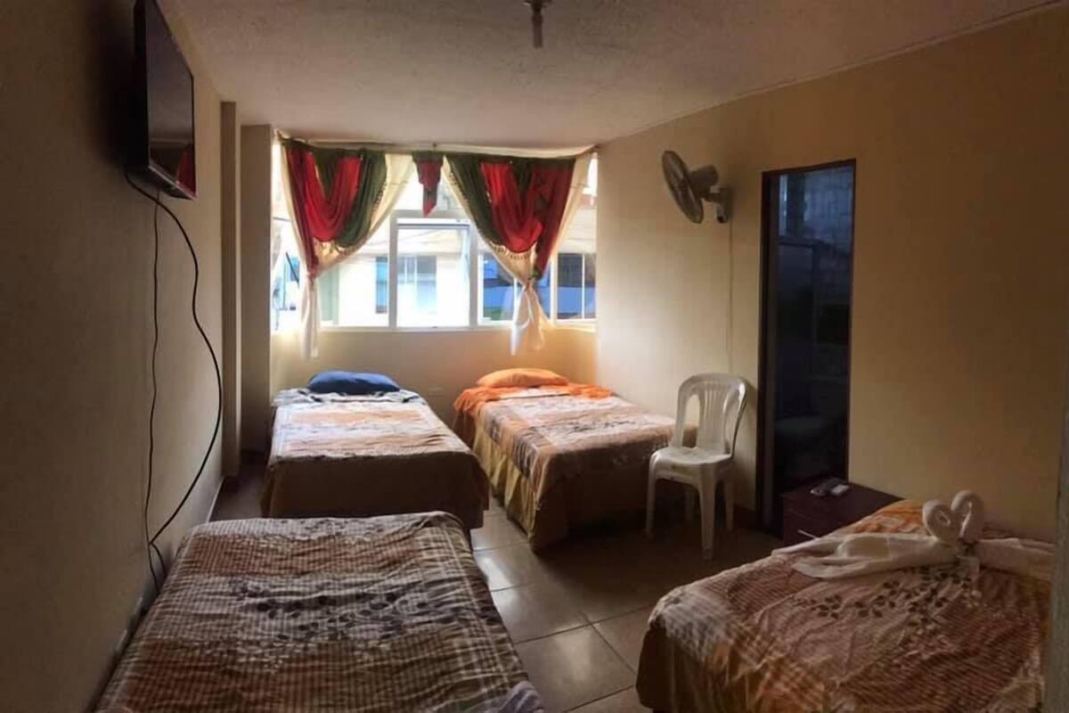 A room with two single beds, a chair, a TV, and a window with curtains.