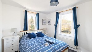 Ein Schlafzimmer mit einem Bett, zwei Nachttischen, einem Fenster mit Vorhängen und einer Deckenleuchte.
