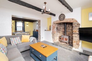 A living room with a stone fireplace, a sofa, a coffee table, and a television. - Spacious Cottage, Parking nr Saunton Sands (Braunton)