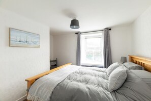 A bedroom with a bed, a bedside table, a lamp, a window with curtains, and a painting on the wall.