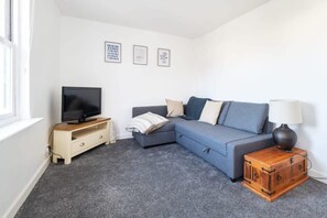 A modern living room with a grey sofa, a television on a wooden stand, and a lamp on a wooden nightstand. - Spacious Cottage, Parking nr Saunton Sands (Braunton)