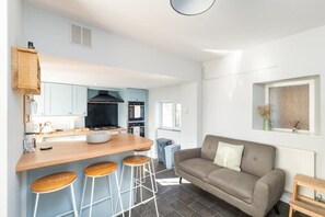 Eine moderne Küche mit Barbereich, einem grauen Sofa und einem Fenster mit Ausblick.