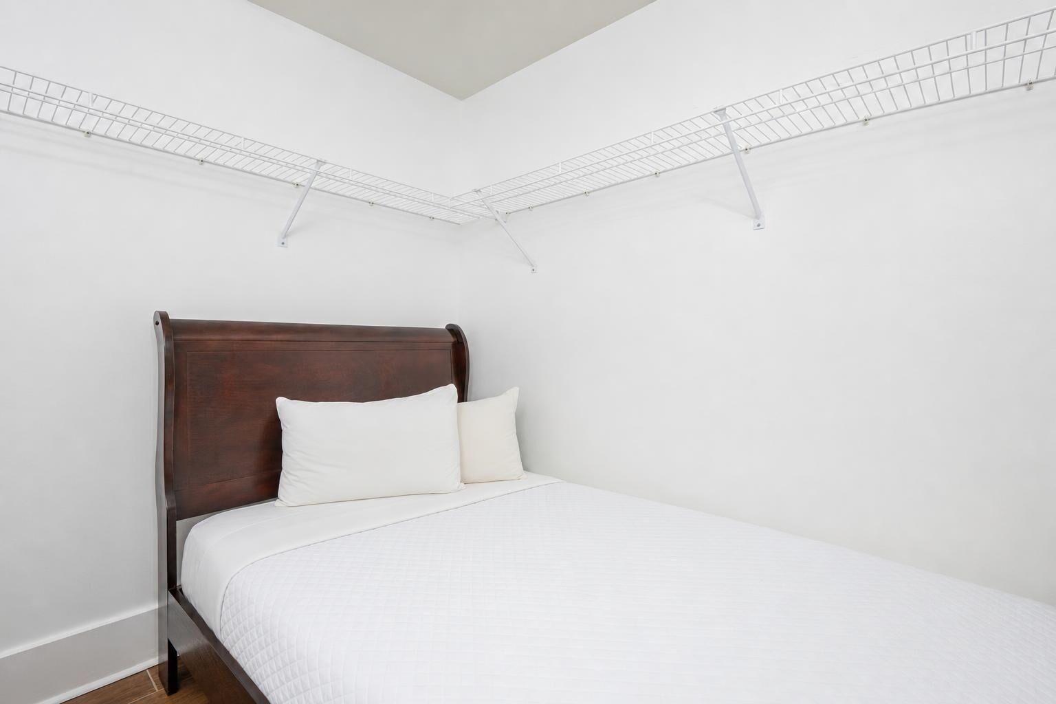 A single bed with a wooden headboard in a room with white walls and a sloped ceiling.