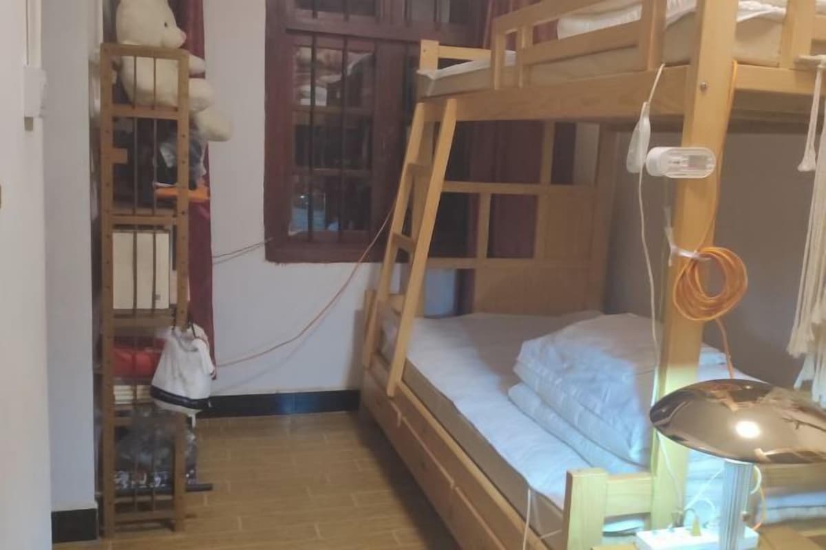 Une chambre avec un lit superposé, une échelle en bois, un petit bureau et une lampe.