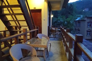 Un balcón con sillas y mesas de mimbre, con vistas a un edificio y una colina.