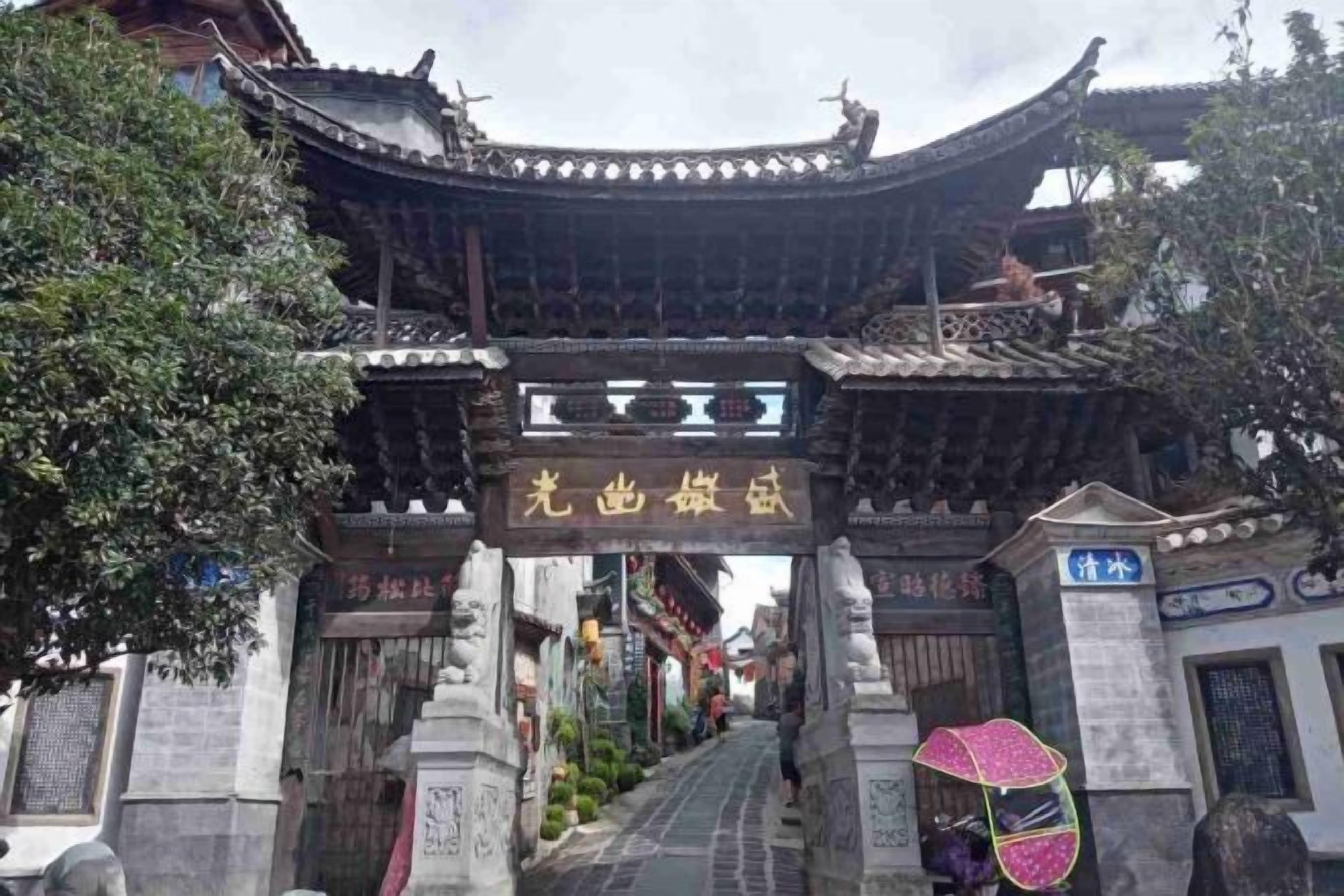 A traditional Chinese gate with a sign, leading to a street with a pedestrian.