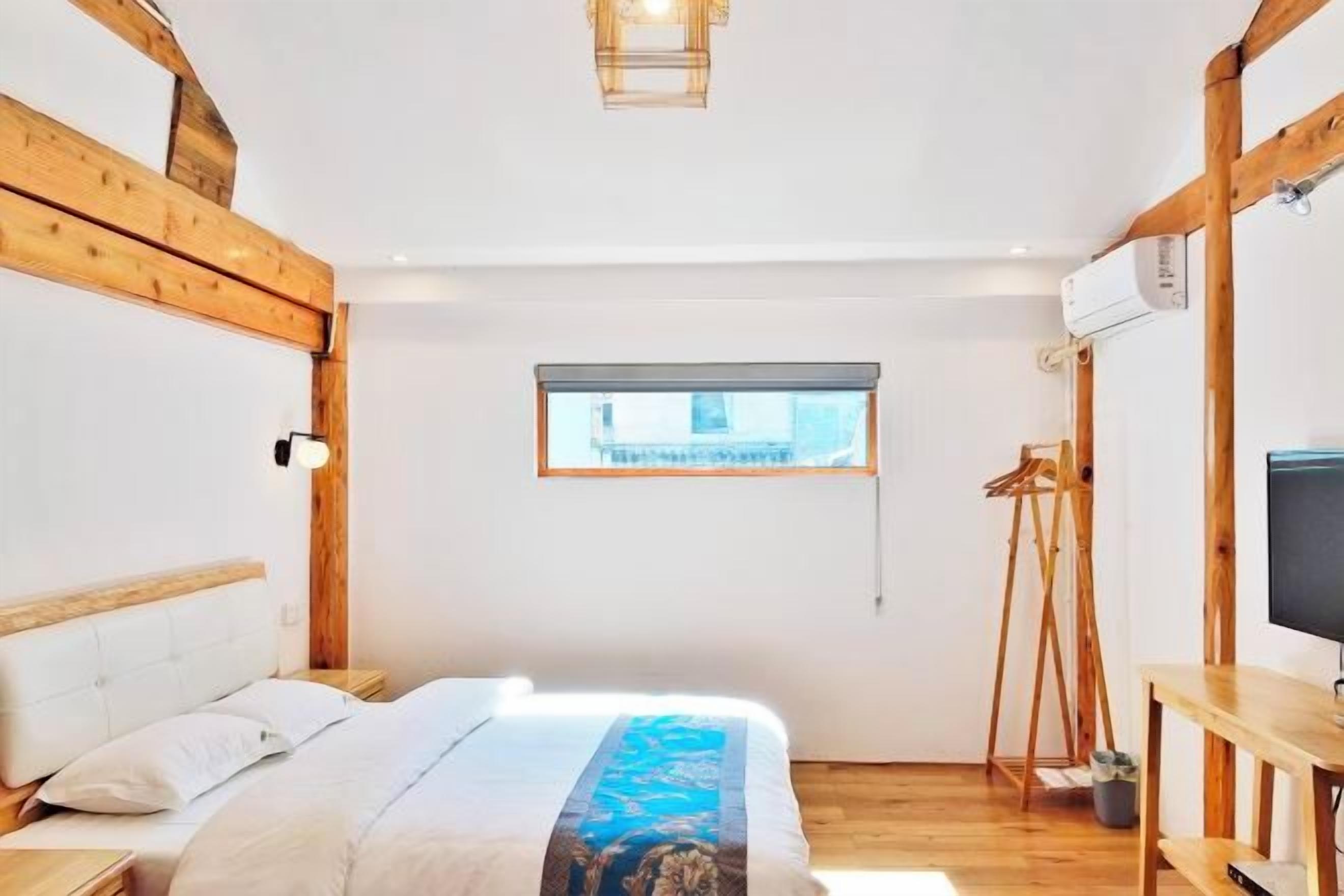 A bedroom with a bed, wooden beams, a window, a TV, and a desk.