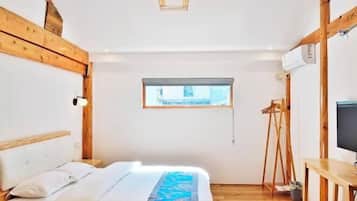 A bedroom with a bed, wooden beams, a window, a TV, and a desk.