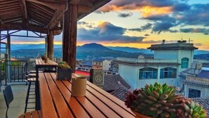 Una terraza de madera con vistas a un paisaje urbano y montañas al atardecer.