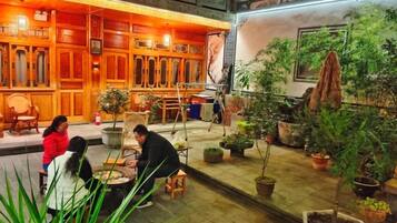 Espacio interior con muebles de madera, plantas en macetas y una persona sentada a una mesa.