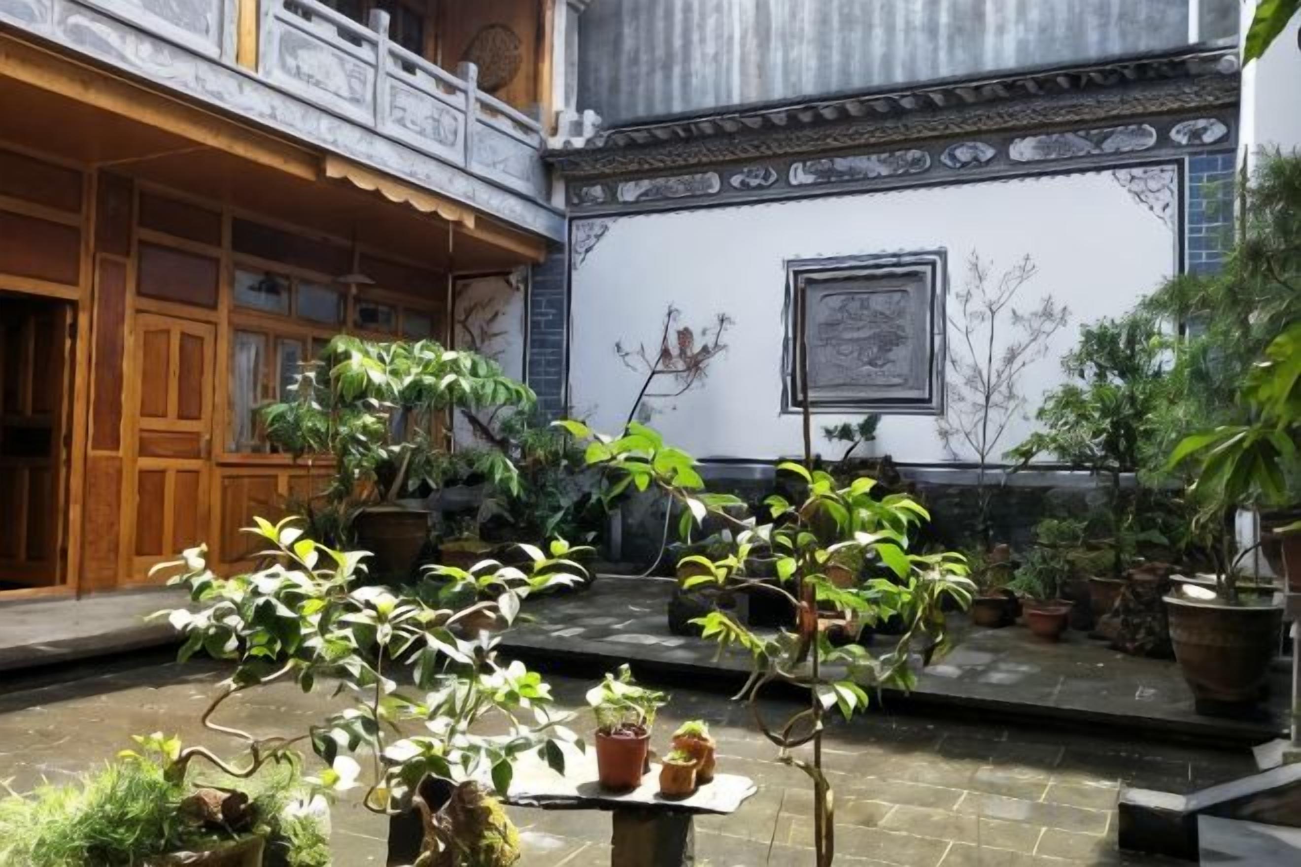 A courtyard with potted plants, a wooden structure, and a tiled wall with a framed picture.
