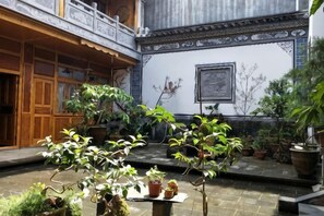 A courtyard with potted plants, a wooden structure, and a tiled wall with a framed picture.