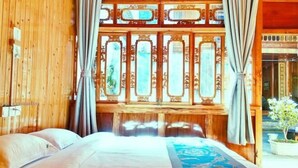 Una habitación con una cama, paredes de madera, un ventanal con paneles decorativos y cortinas.