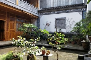 Ein Innenhof mit Blumentöpfen, einer Holzhütte und einer mit Kacheln verkleideten Wand mit einem gerahmten Bild.