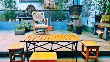 An outdoor patio with a wooden table and chairs, surrounded by potted plants and a stone bench.